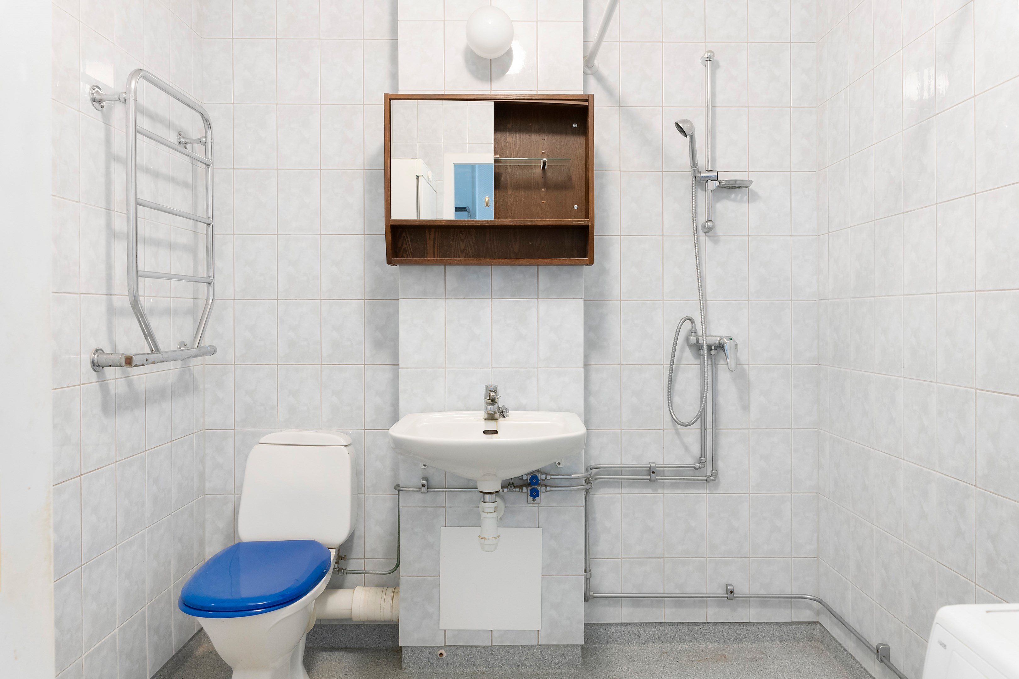 Luftigt badrum med plats för dusch, tvättmaskin och torkskåp.