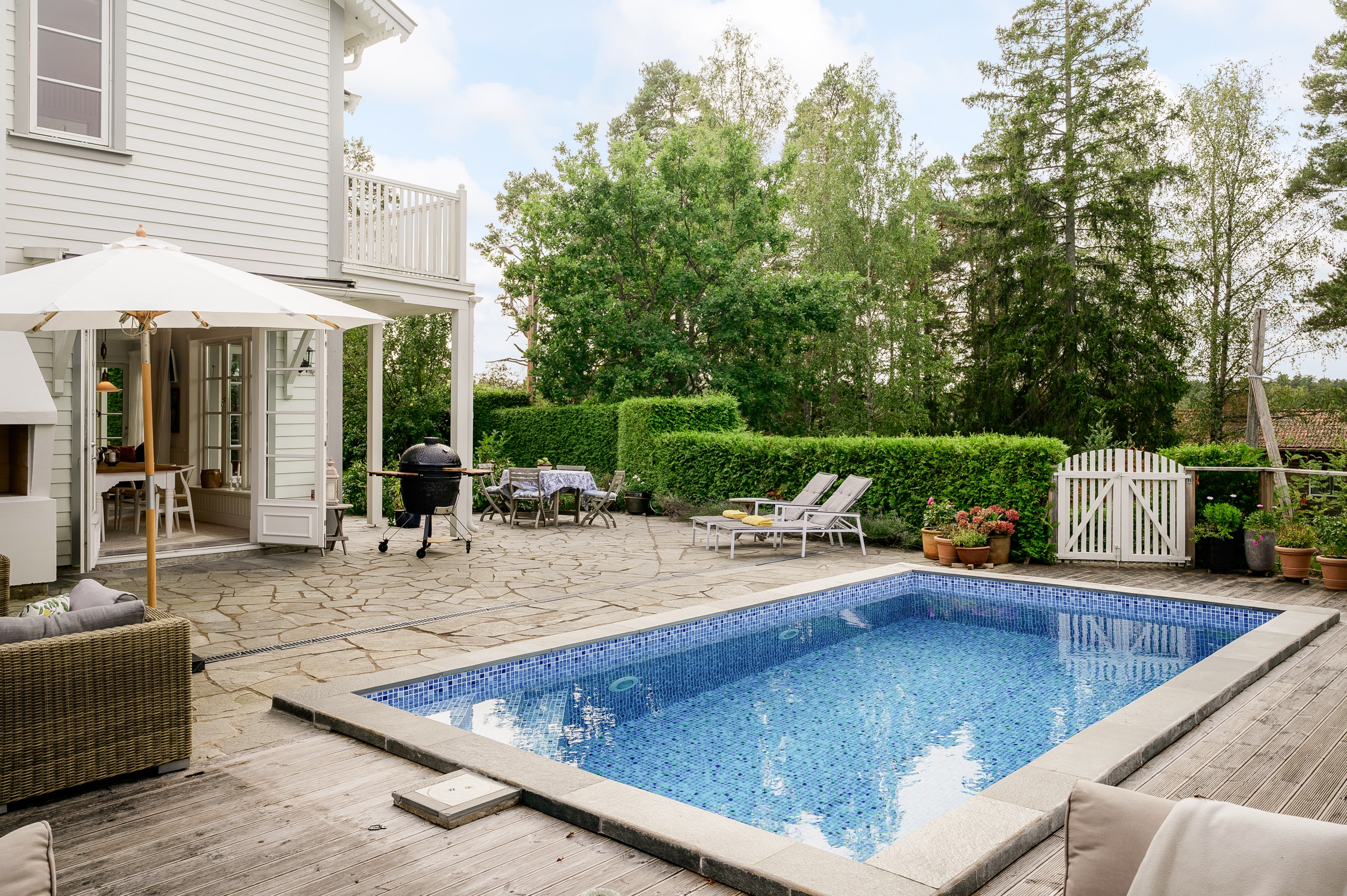 Poolområde med högt fritt sydvästläge inramad av uppvuxen grönska.