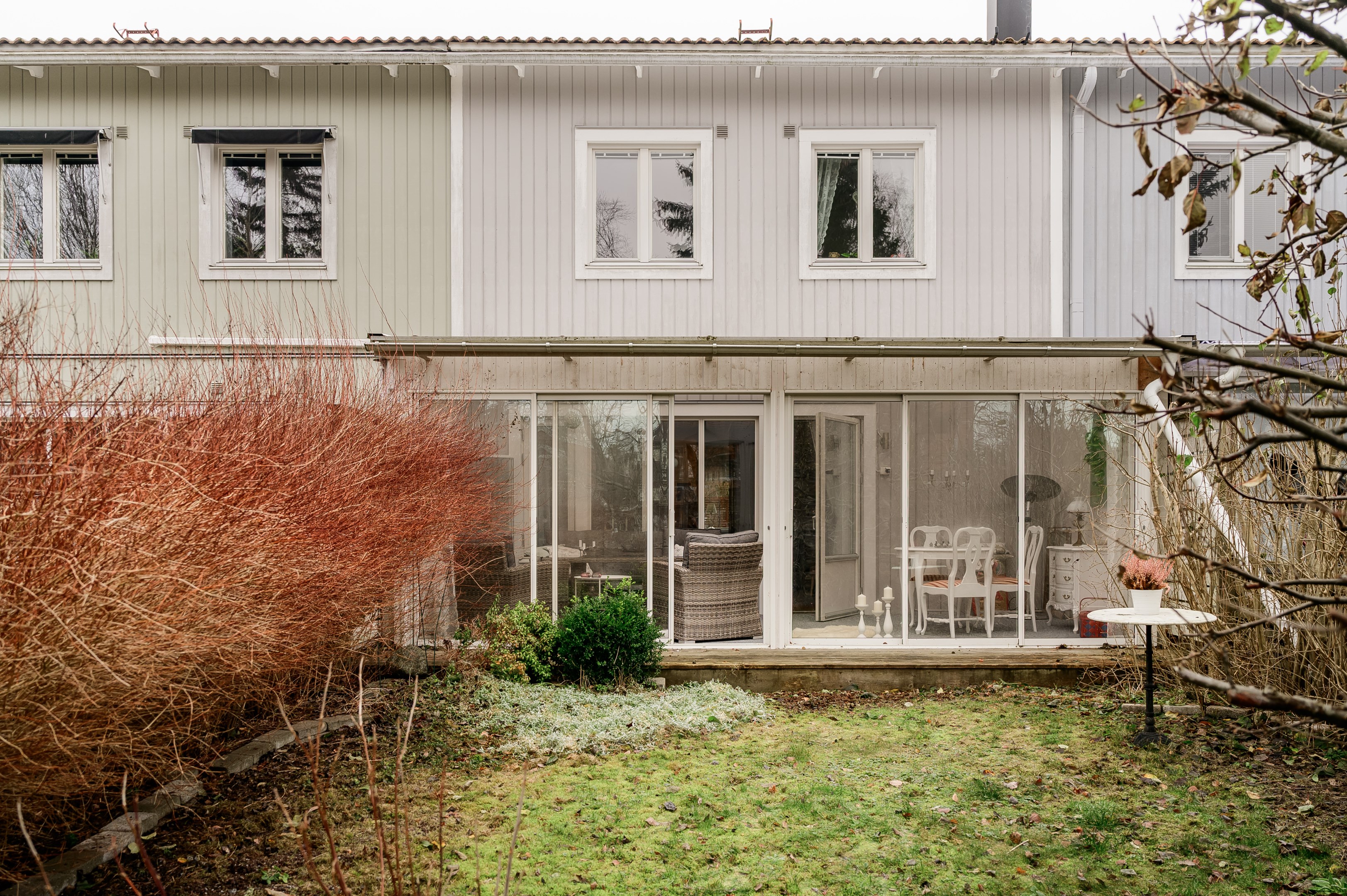 Baksida med plana gräsytor inramad av uppvuxen grönska.