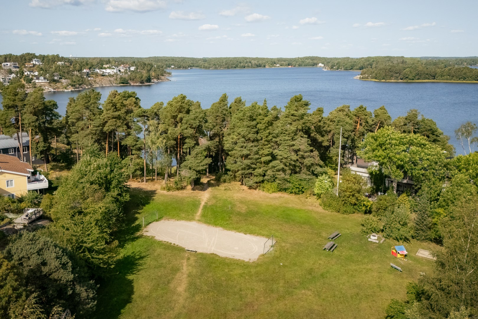 Allmänning med plana grönytor och lekplats i nära anslutning til badplatsen.
