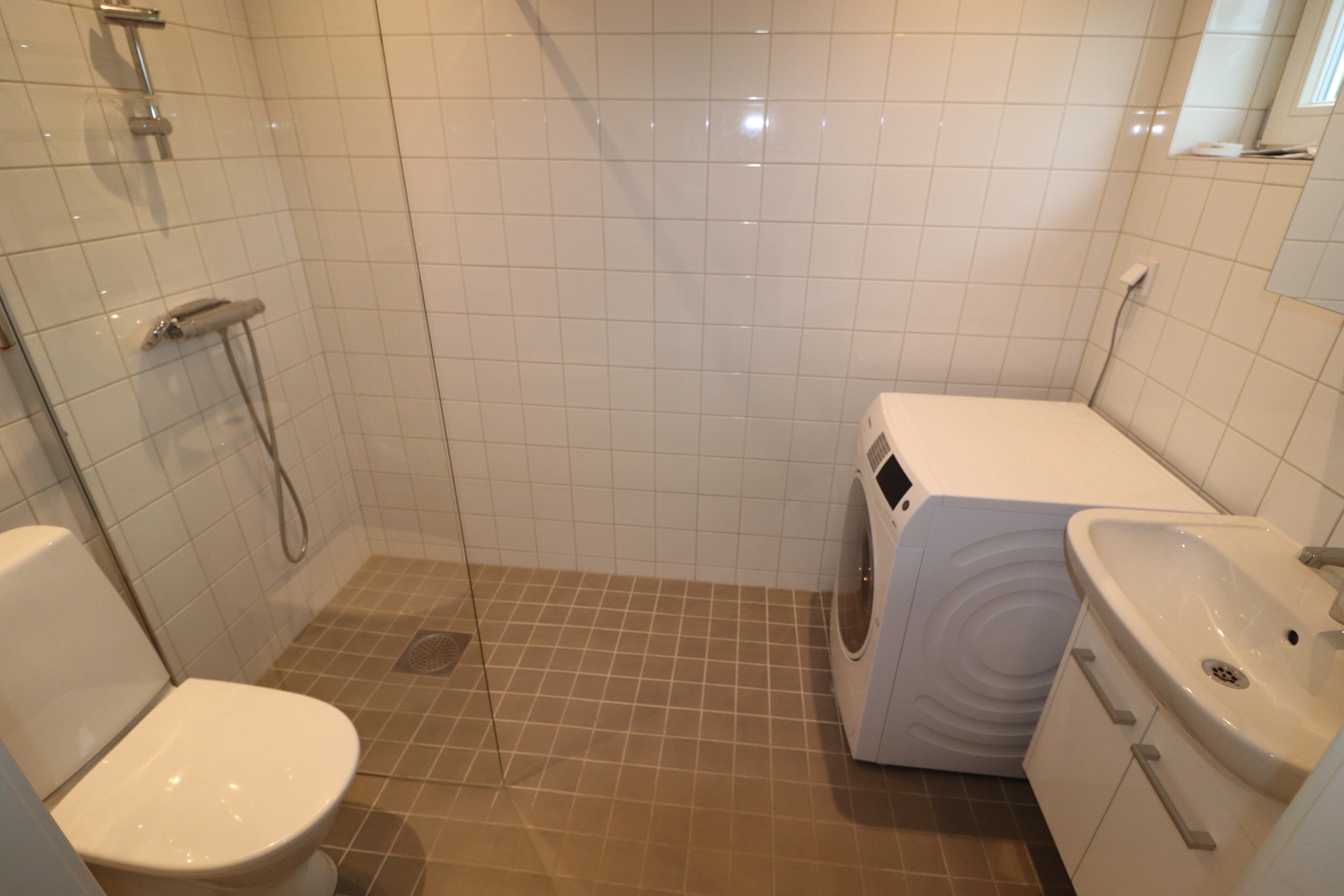 Kaklat badrum med dusch och tvättmaskin