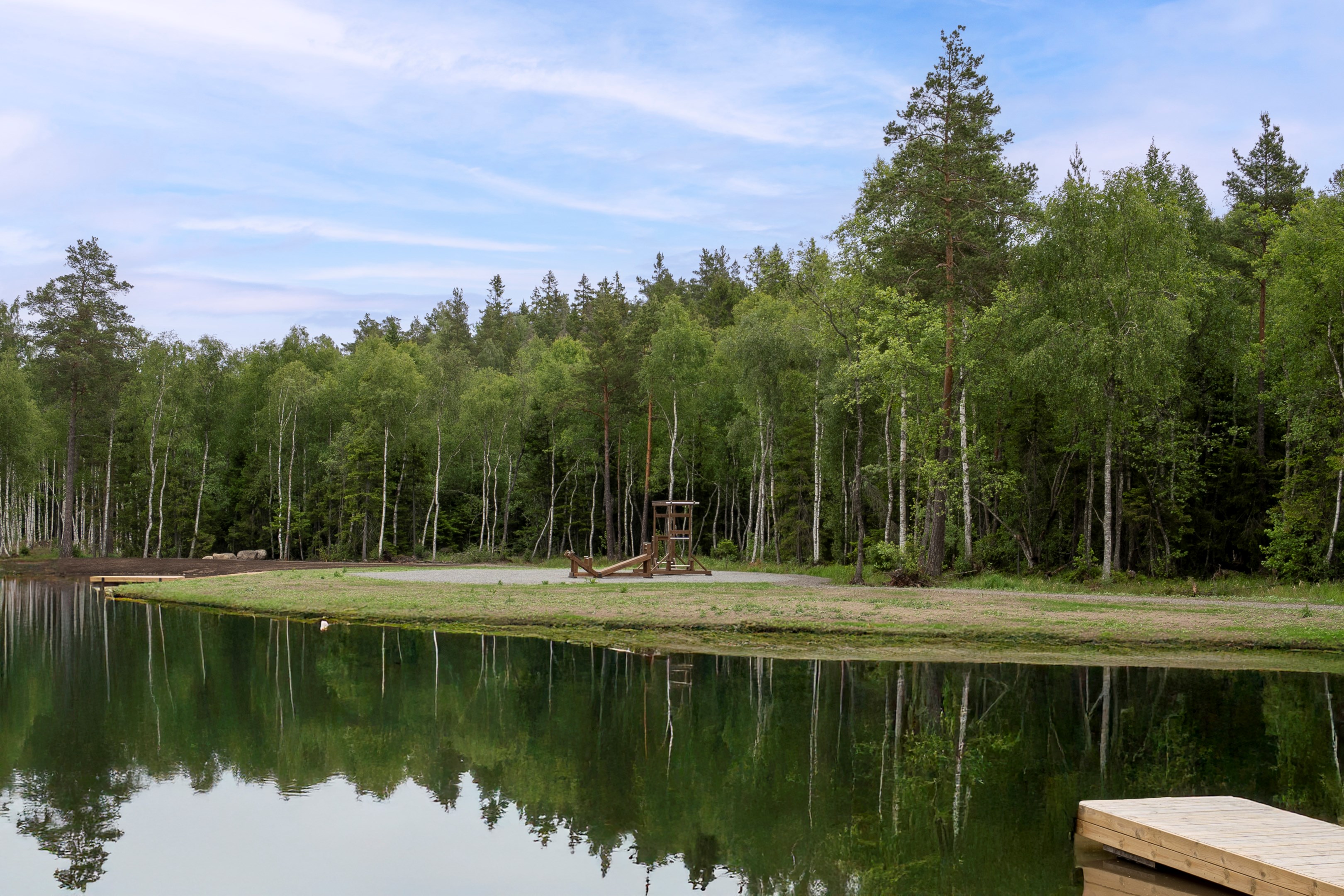 Områdesbild, anlagd liten sjö i närheten av fastigheterna som är till salu.