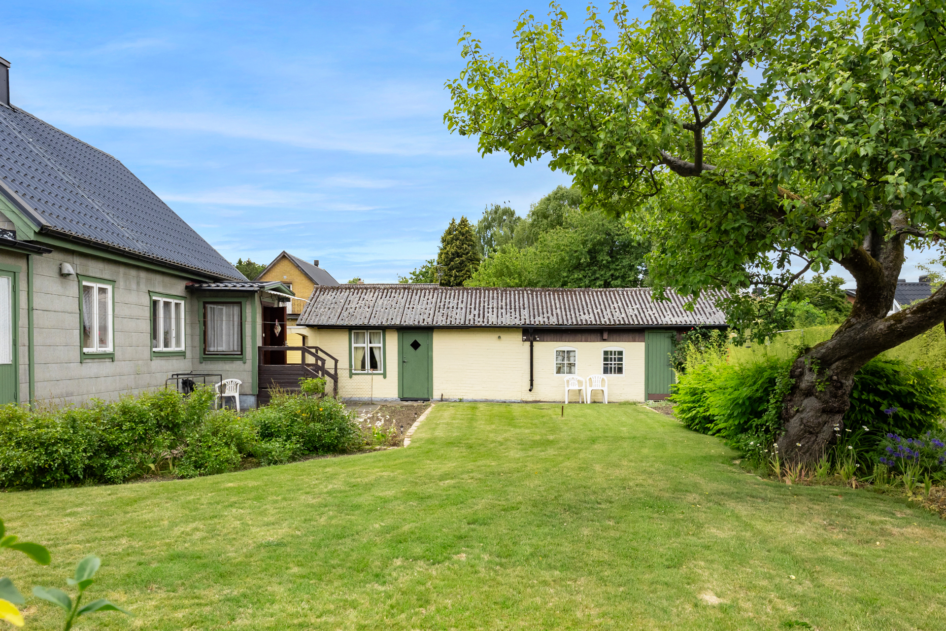 Trädgård med vy mot garage och förråd